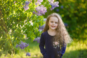 Outside portrait of a beautiful girl with long curly hair near lilac bushes