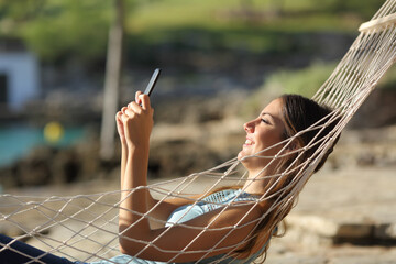 Happy woman checking phone on a hammock on the beach
