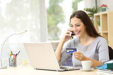 Happy woman talking on phone holding card at home
