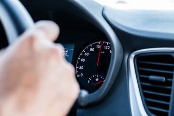 closeup of a hand on steering wheel and speedometer in the background  