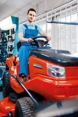 Fototapeta na wymiar Male worker sitting on lawn mower in tool store