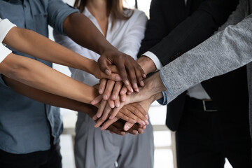 Close up diverse colleagues stacking hands, showing unity and support, successful employees team celebrating achievement, sharing success, engaged in team building activity at briefing