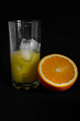glass of freshly squeezed orange juice with ice on black background
