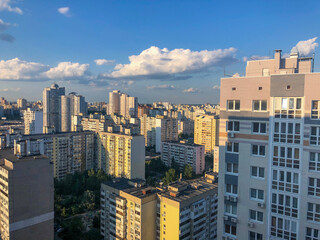 Fototapeta premium view from the top of the city on residential blocks of high rise buildings across blue sky and white clouds. Building infrastructure 