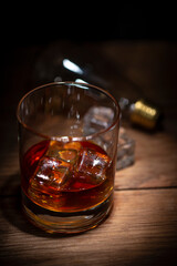 A glass of whisky with ice cubes on wooden background