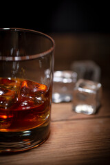A glass of whisky with ice cubes on wooden background