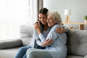 Happy multi-generational family sitting on couch in living room, elderly grandmother snuggle to...