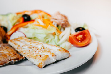 Sea bass fish steak golden grilled with fresh salad on white plate and white background