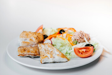 Sea bass fish steak golden grilled with fresh salad on white plate and white background