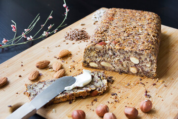 Healthy homemade keto bread with almonds, hazelnuts, sunflower seeds, chia seeds on a wooden cutting board.