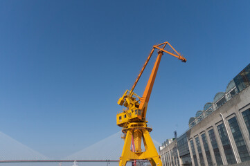 Fototapeta na wymiar Yellow orange color crane in the sunny day with clear sky as the background. Brand new high lifter in the construction site in the background of the blue sky. Look up from the bottom on the ground.