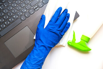 woman's hand in a blue rubber glove with white cloth wipes the keyboard of a laptop. concept of home cleaning and order