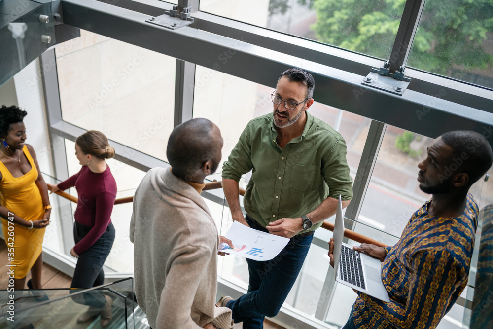 Wall mural Diverse businesspeople talking together on stairs in an office staircase