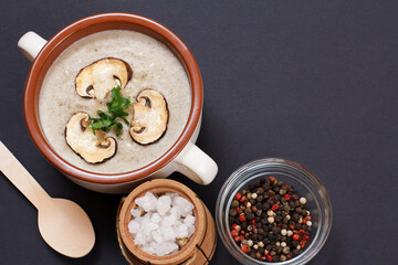 Cream soup with mushrooms in porcelain bowl with spoon and spices on black background.