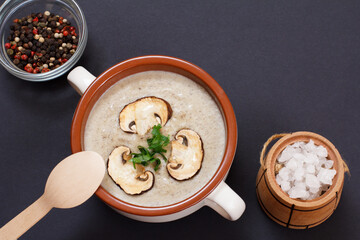 Cream soup with mushrooms in porcelain bowl with spoon and spices on black background.