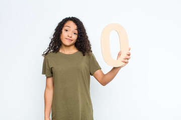 young pretty latin woman confused, doubtful, thinking, holding a number 0.