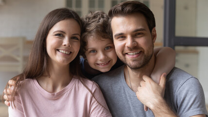Headshot portrait of happy young family with little preschooler son hug and cuddle posing looking at camera together, smiling parents embrace small boy child relax on weekend at home, bonding concept