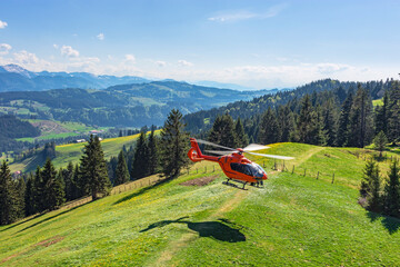 Red rescue helicopter of the German Luftrettung landing on a green hilltop. Allgäu, Bavaria, Germany © Andreas Föll