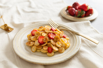 Mini pancake cereal with strawberries for breakfast on light table. Tiny pancakes, new food trend during Covid-19 lockdown. Cute healthy breakfast or snack. Recipe, menu