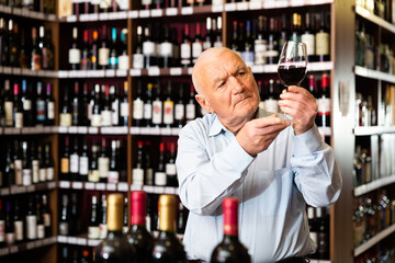 Portrait of senior man tasting red wine at wine shop