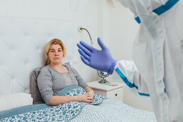 Doctor wearing a PPE attends a woman with COVID in the bed at home