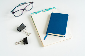 on a white table lies a sketchbook and a notebook, next to glasses and paper clips