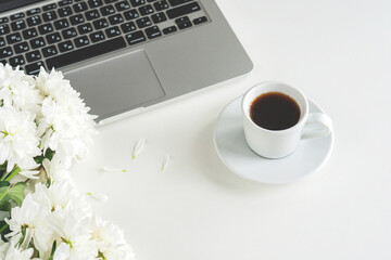 a coffee mug and a laptop stand on a table, white flowers lie nearby