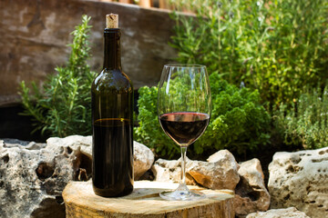Botella de vino tinto junto a una copa con vino al aire libre. Vista de frente