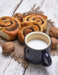 Basket of homemade buns with jam, served on old wooden table with walnuts and cup of milk