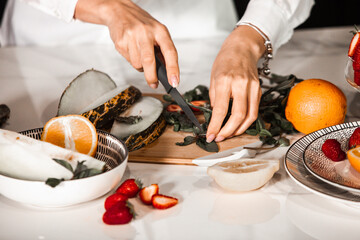 Closeup on woman making fruits salad. Preparing a healthy spring fruit salad. Happy healthy woman cutting fruits on a wooden board. exotic fruits