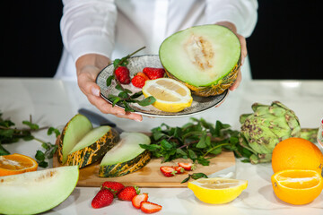 Closeup on woman making fruits salad. Preparing a healthy spring fruit salad. Happy healthy woman cutting fruits on a wooden board. exotic fruits