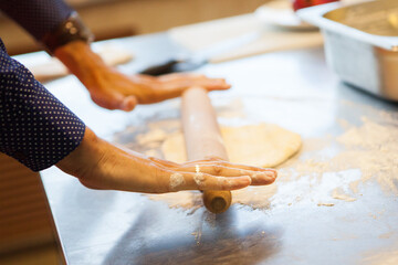 Female hands roll out the dough with a rolling pin.