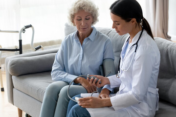 Female physician caring about old woman manually takes blood pressure using sphygmomanometer seated...