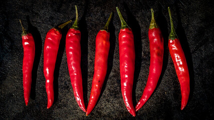 top view of a group of 7 red wrinkled chili peppers lined side by side on a cast iron surface