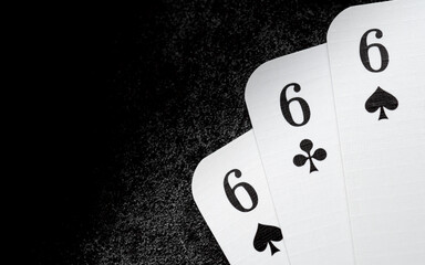 white playing cards 666 six of spades and six of clubs in the right lower corner on black cast iron surface with copy space at the left side, three of a kind, triple six
