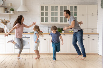 Naklejka premium Overjoyed young family with little children dancing enjoying leisure weekend in kitchen, happy parents have fun feel playful engaged in funny activity with small kids at home, entertainment concept