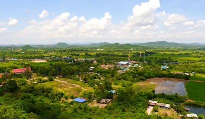 Residential buildings and green forest in aerial view. Landscape of village in the valley and beautiful blue sky with fluffy white clouds in a day.