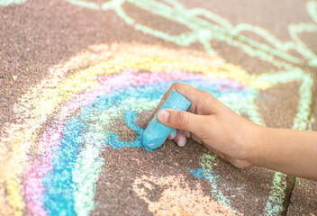 Kid painting a rainbow with a sidewalk chalks. Summer outdoor activity for children idea.