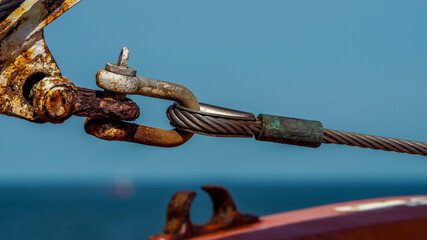strong link of a twisted wire rope is attached to a rusty shackle of a nautical vessel offshore in...