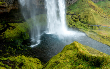 Fototapeta na wymiar view of the popular magical Seljalandsfoss waterfall cascading into a small pond surrounded by a footpath trough green grass, nearby Storidalur, iceland