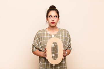young pretty woman confused, doubtful, thinking, holding a number 0.