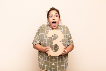 young pretty woman surprised, shocked, amazed, holding a number 3.