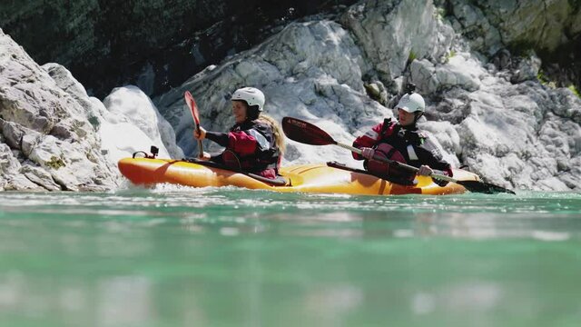 Slow motion close up two people kayaking in dual kayak on emerald whitewater river, over rapids, enjoying nature Soca, Slovenia