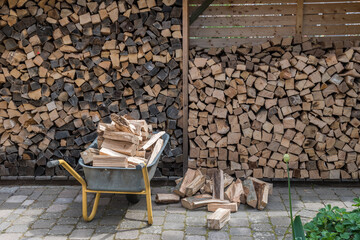 Stacked pile of firewood and a wheelbarrow with pieces of fire wood to be stockpiled