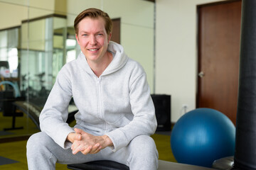 Fototapeta premium Happy young handsome man with hoodie smiling and sitting at the gym