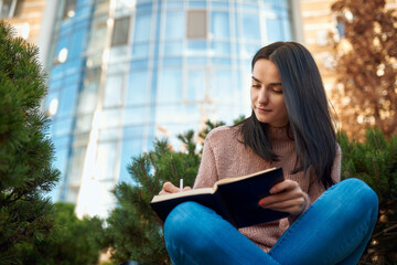 Lovely lady doing written work on a lawn in front of tall building