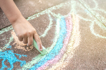 Kid painting a rainbow with a sidewalk chalks. Summer outdoor activity for children idea.