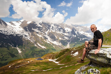 Man on top of mountain. Conceptual design. An elderly man sits on top of a mountain. Active holiday in retirement. Time is one with itself. Mountain landscape in the Alps.