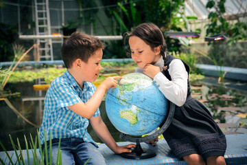 two school children look at the globe against the background of the winter garden