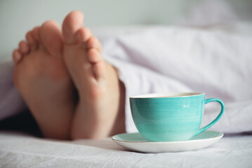 Fototapeta na wymiar Cup of coffee or tea and female legs under a blanket close up. Woman morning.